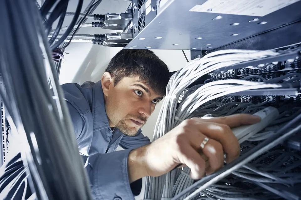 A technician reaches into a server rack to work on a bundle of network cables.