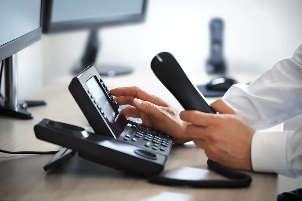 Hands lifting the handset of a desk IP phone and dialing on its keypad.
