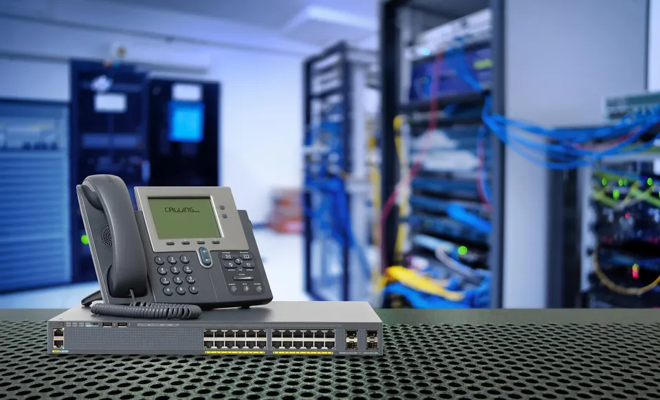 A desk IP phone and a network switch in front of rows of server racks.